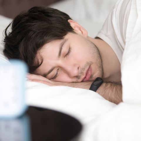 Young man sleeping next to alarm clock wearing smart wristband