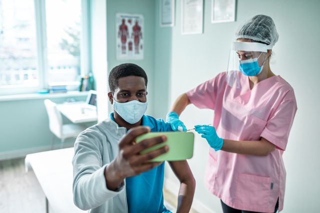 young man taking a selfie while getting vaccinated