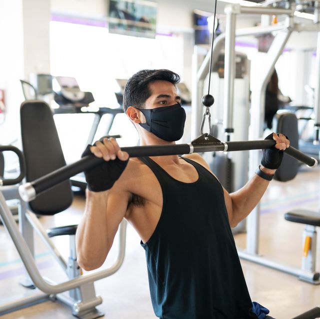 young man with a mask exercising in the cable machine