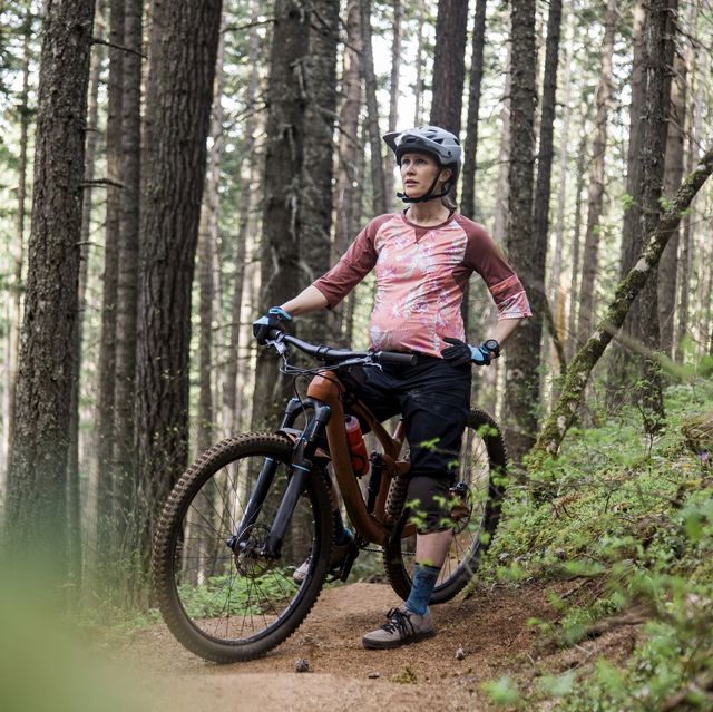 a young pregnant woman mountain bikes on a trail in the forest of oregon