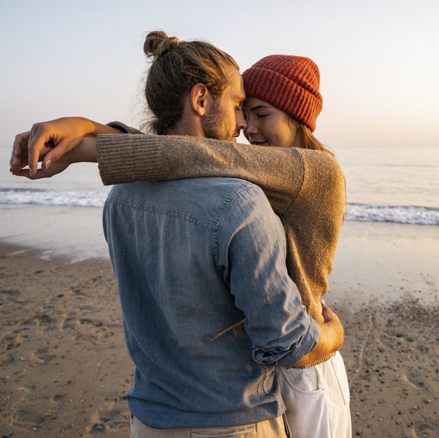 young romantic couple standing face to face at beach against clear sky during sunset