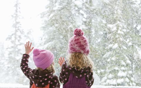 young sisters look at snowfall outside