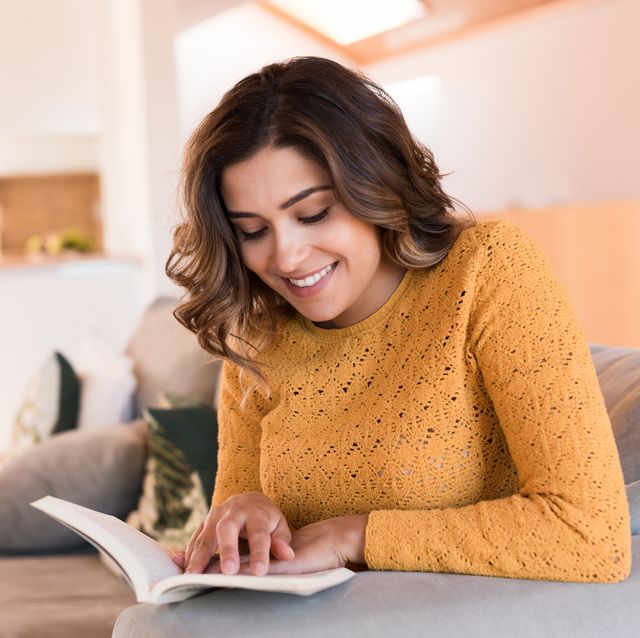 young smiling woman reading book while sitting at home