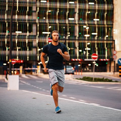 young sporty man jogging through city streets with backpack on back