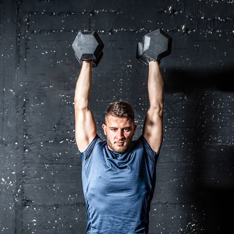 Young strong fit muscular sweaty man with big muscles strength cross workout training with dumbbells weights in the gym dark image with shadows real people