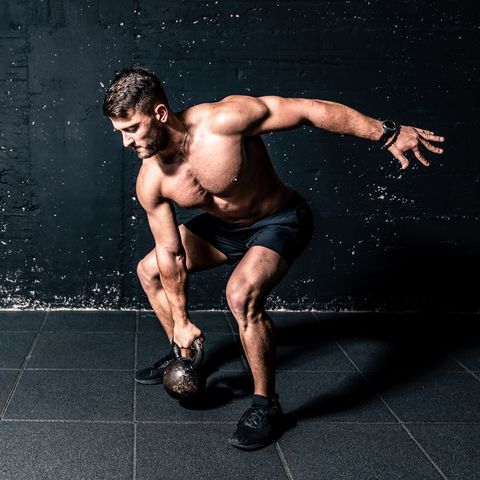 Young strong sweaty focused fit muscular man with big muscles holding heavy kettle bell for training hard core workout in the gym real people