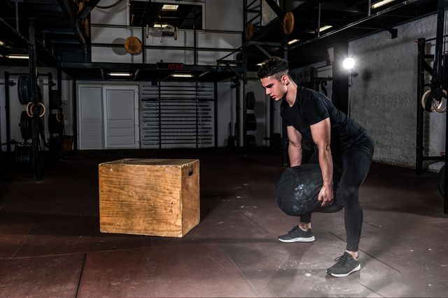 young sweaty strong fit muscular man picking up and hold with his hands heavy sand bag weight for strength cross workout training in the gym