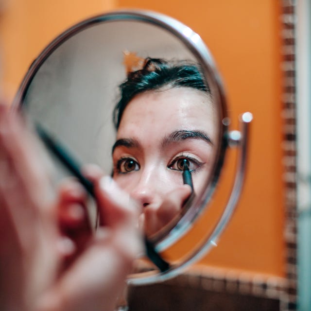 young teenager applying eyeliner in domestic bathroom