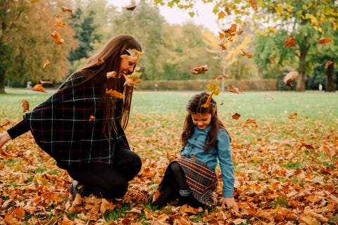 Young woman and little girl playing with autumn leaves on a meadow