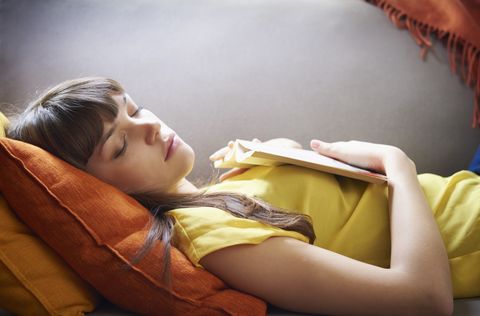 Young woman asleep with book on sofa