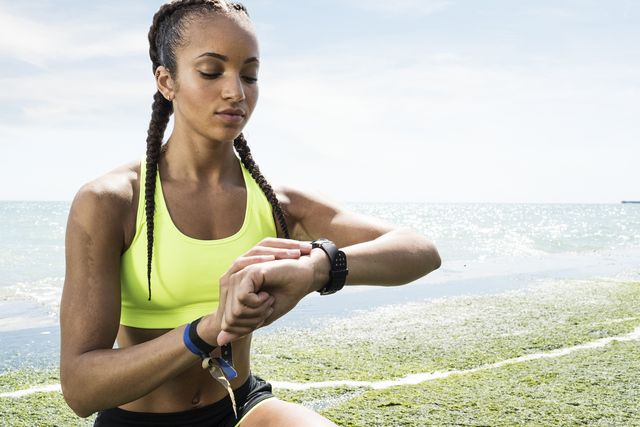 young woman beside sea, wearing sports clothing, looking at activity tracker