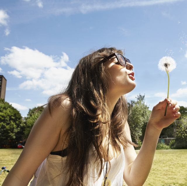 young woman blowing away the dandelion seeds