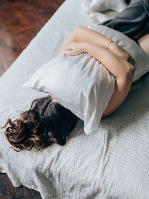 young woman covering face with pillow on bed