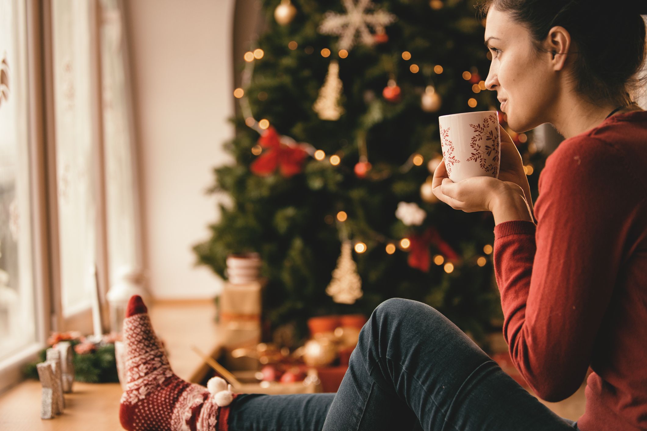 νεαρή γυναίκα που πίνει τσάι δίπλα στο χριστουγεννιάτικο δέντρο