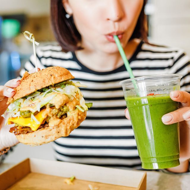 a young woman drinks green smoothies and eats a burger in a vegan fast food restaurant