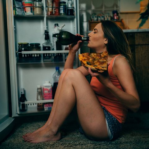 Young woman eating and drinking in the kitchen late night