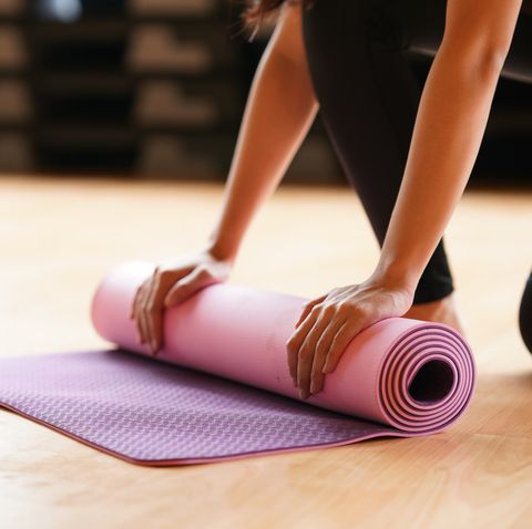 young woman folding yoga mat  after class end