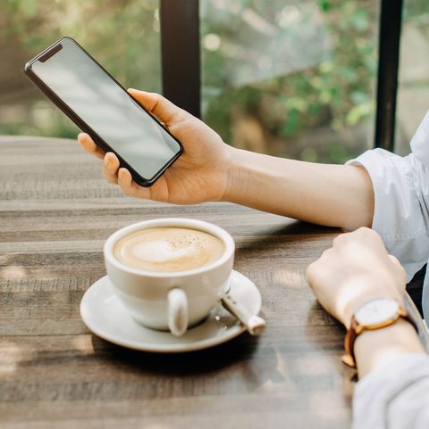 Young woman having a relaxing time in cafe, enjoying coffee while using smartphone