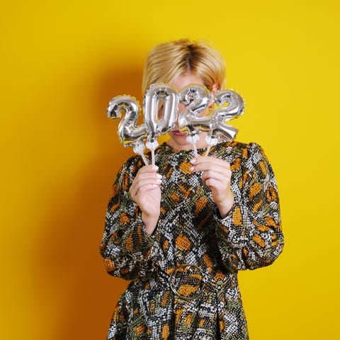 Young woman hiding behind 2022 number balloons. new years colors yellow 2022