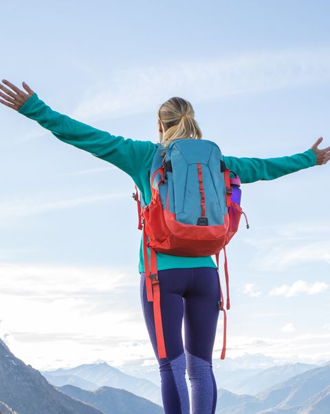 Young woman hiking reaches mountain top, outstretches arms