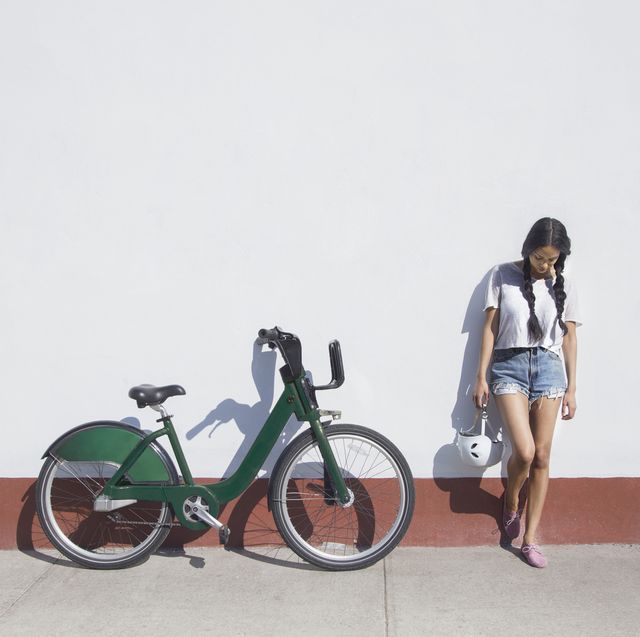 young woman holding helmet while standing by bicycle on sidewalk