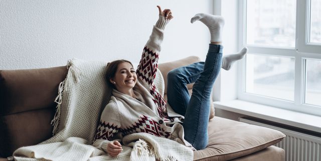 young woman in a sweater lies on the sofa by the window
