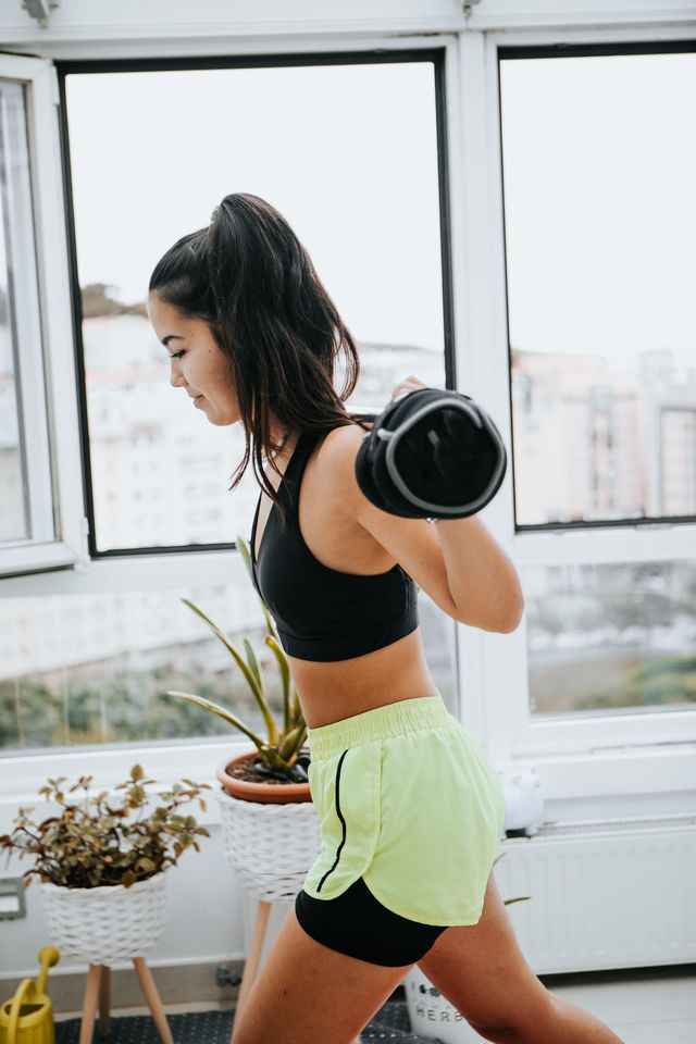 young woman in casual clothes doing exercise with dumbells at home
