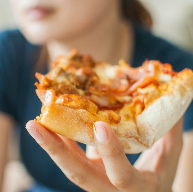 a young woman is spending her time eating a slice of pizza white sitting on a couch
