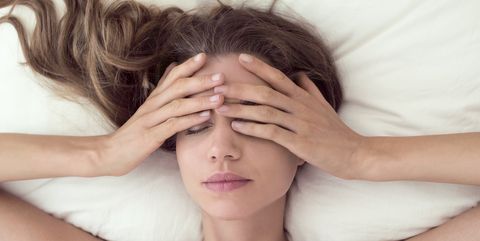 young woman lying in bed and covering eyes