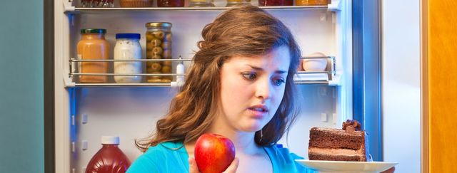 young woman making decision on healthy eating in front of refrigerator