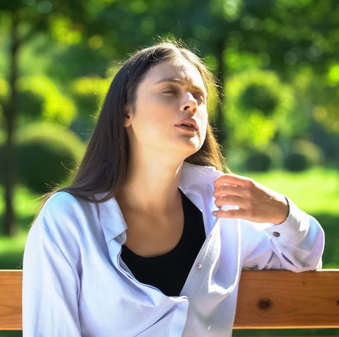 young woman resting on bench in park suffering from heat and stuffiness, pms