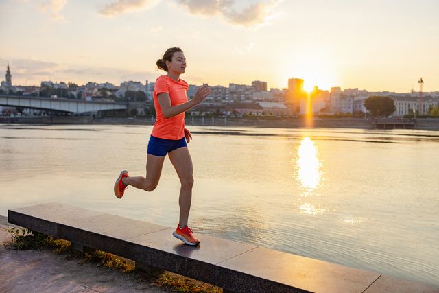 young woman running on platform by the city river, jogging at sunset