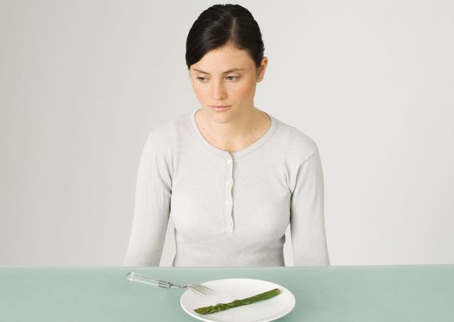 Young woman sitting in front of plate with single asparagus, looking away