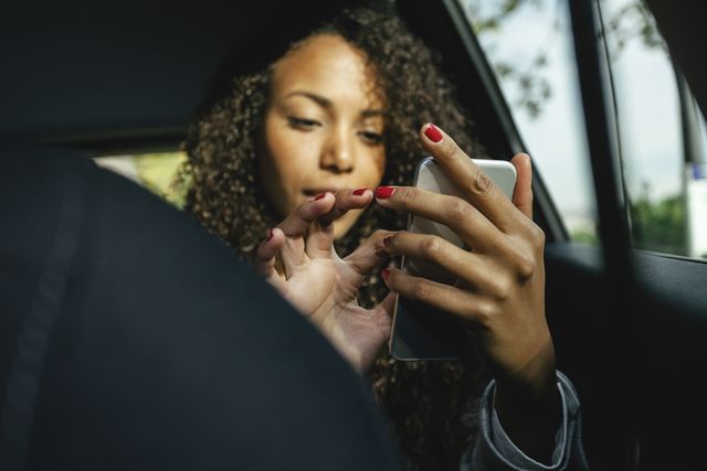 young woman sitting on back seat of a car using smartphone
