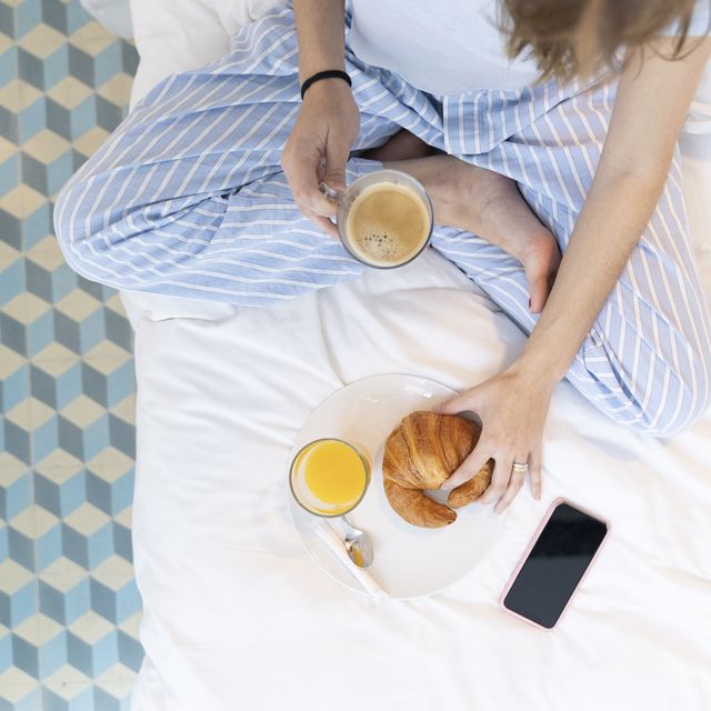 young woman sitting on bed and having a coffee