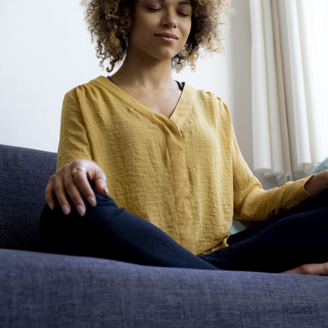 Young woman sitting on couch at home meditating