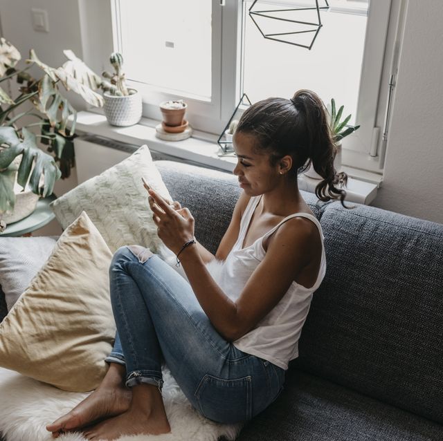 young woman sitting on the couch at home using mobile phone