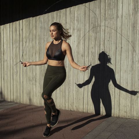 young woman skipping while exercising against wall