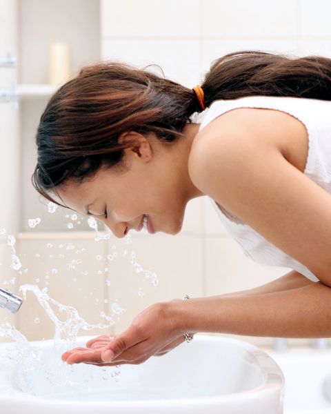 young woman splashing water on face in bathroom