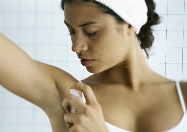 young woman spraying underarm, head and shoulders