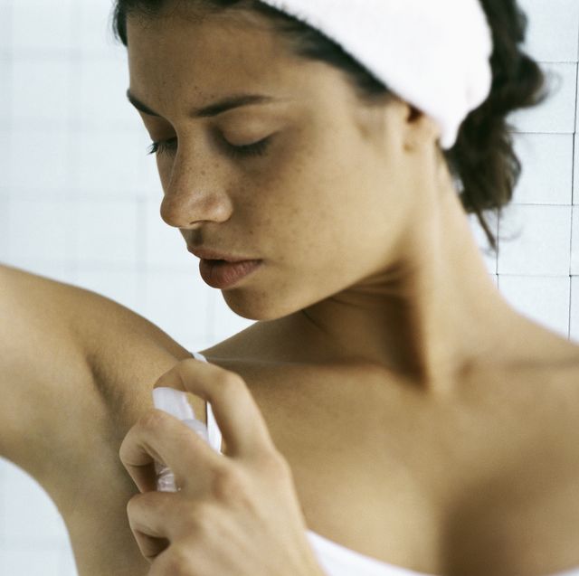 Young woman spraying underarm, head and shoulders