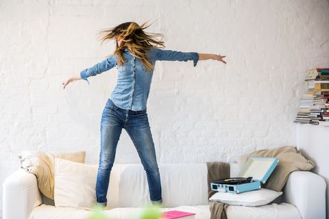 Young woman standing on sofa dancing and shaking her hair