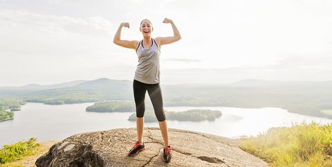 Young woman standing on top of mountain and flexing muscles