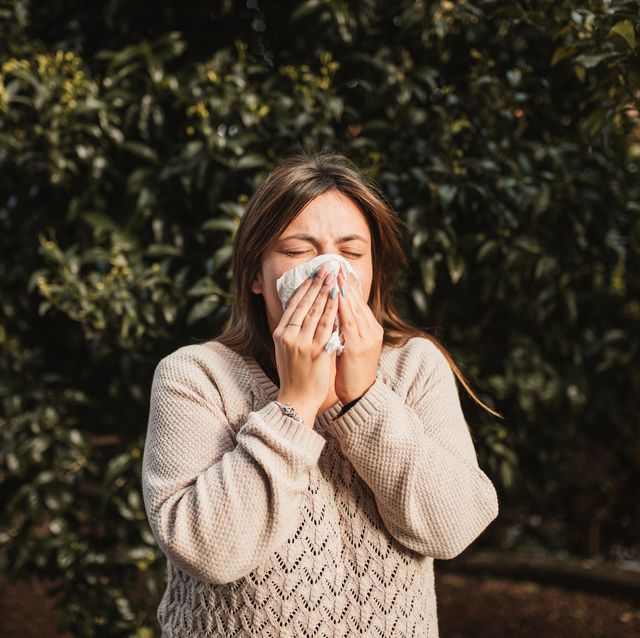 young woman suffering spring allergy and blowing nose with a tissue in the nature
