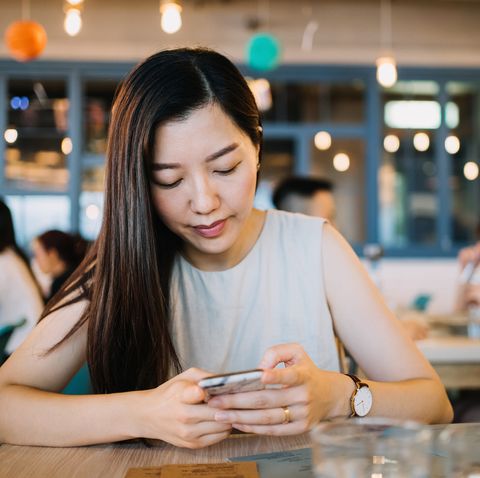 young woman text messaging on smartphone while waiting for her meal in the restaurant