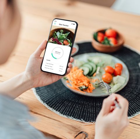 young woman using calorie counter app on smartphone while eating salad