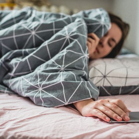 A young woman wakes up the bed. the alarm on the smartphone is ringing