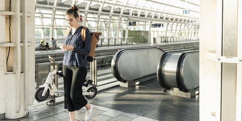 young woman with electric scooter and cell phone at the train station