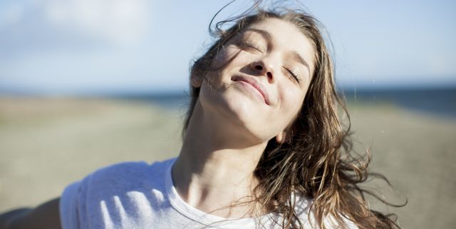 young woman with eyes closed smiling on a beach