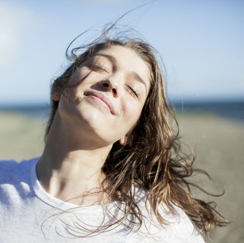 young woman with eyes closed smiling on a beach